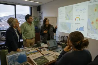 Small group of diverse professionals in a city office thoughtfully studying environmental data and real-time dashboards, afternoon light, authentic and candid mood